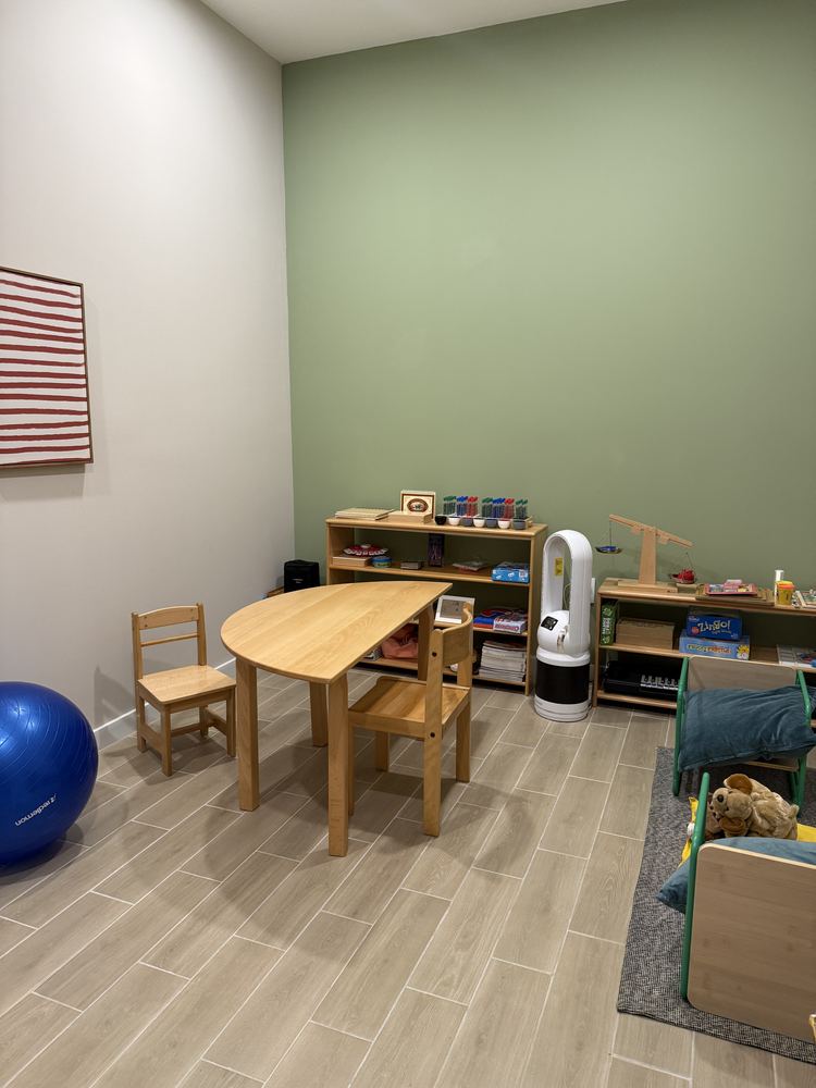 Consultorio de pedagogía: mesa y sillas infantiles, repisas con material y muro verde.
