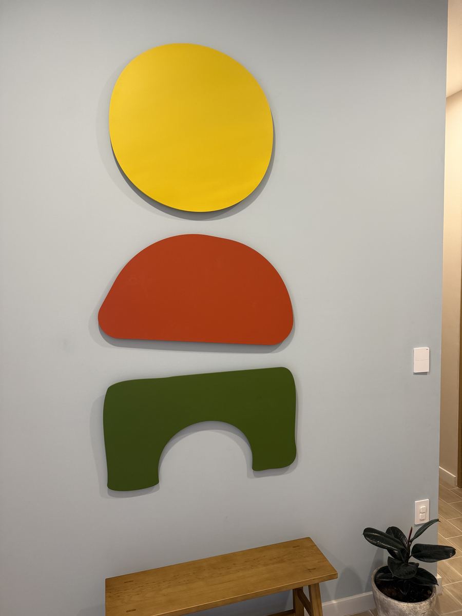 Las tres formas del símbolo de PIAOL —círculo amarillo, cúpula coral y arco verde— montadas en un muro del centro, sobre una banca de madera.
