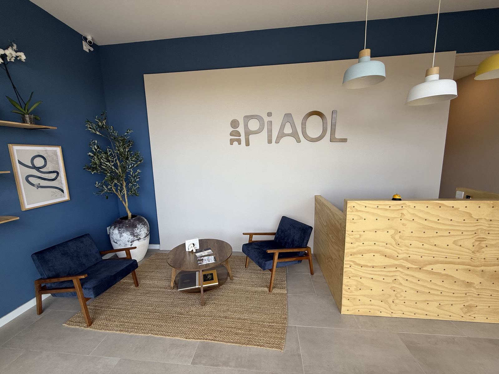 Recepción y sala de espera: muro azul con un olivo, dos sillones y el logotipo de madera.