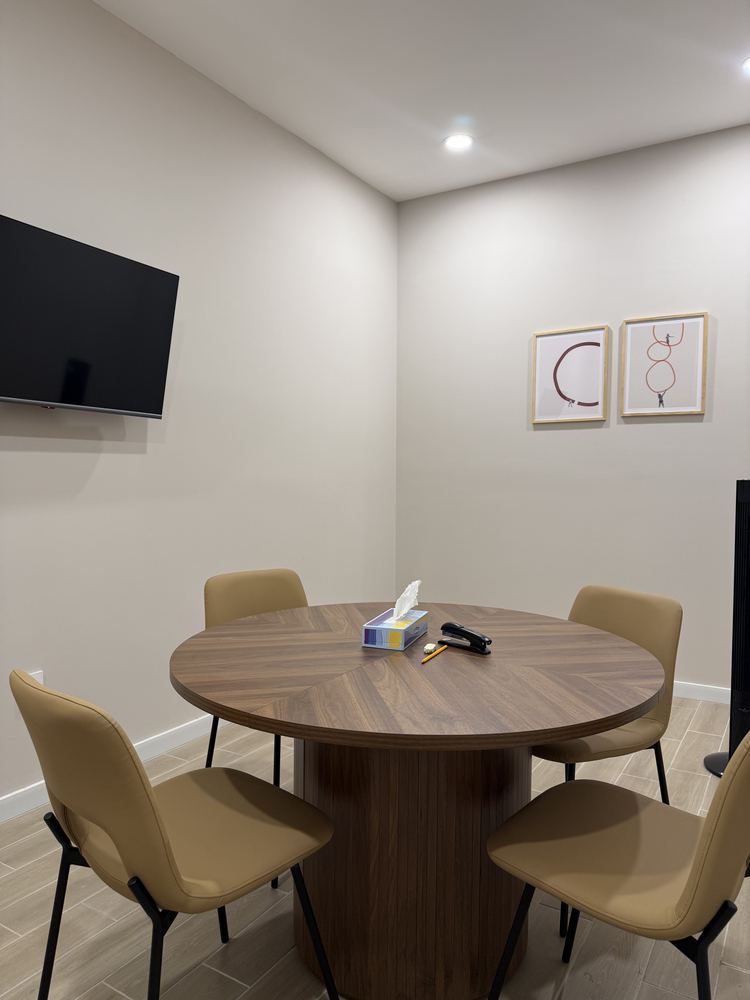 Sala donde ocurre la primera cita: mesa redonda con cuatro sillas y pantalla en la pared.